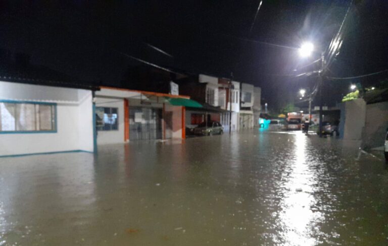 1. Calle inundada por fuertes lluvias en Huila, calles con agua estancada, daños en infraestructura y vehículos parcialmente sumergidos en la noche.