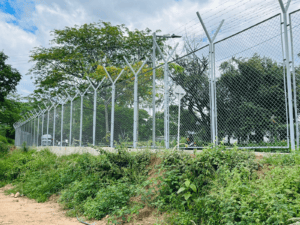 Valla de seguridad metálica en área rural de Huila, Colombia, rodeada de vegetación y árboles, con cielo parcialmente nublado, protección y control de acceso en zonas estratégicas de la región.