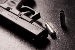 Arma de fuego y un cartucho de bala en superficie negra, concepto de seguridad y violencia.