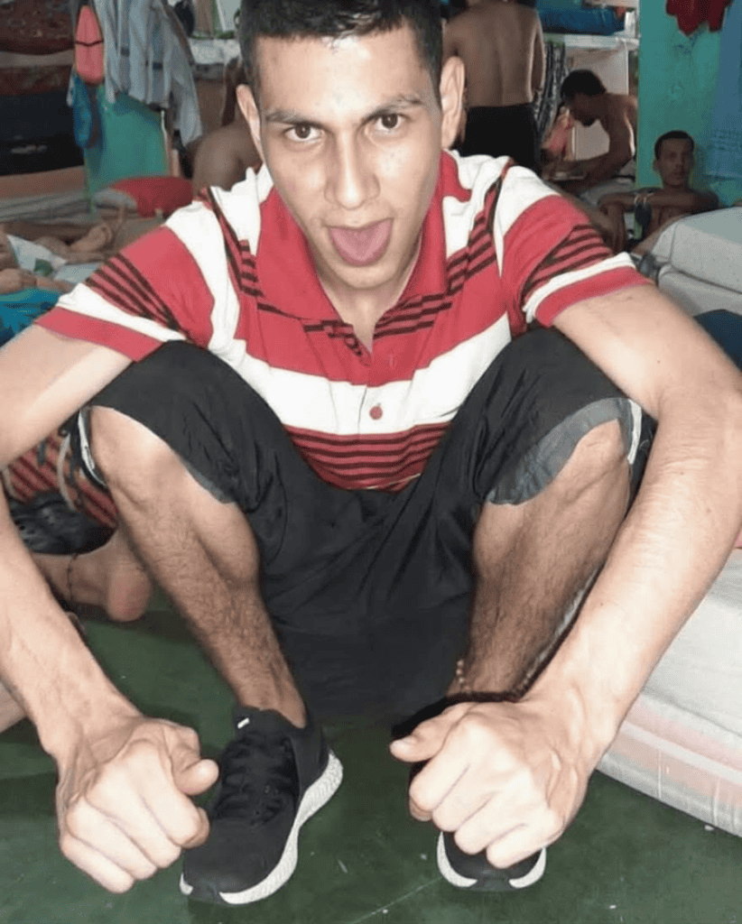 Hombre joven en una pose dinámica en un entorno social, con fondo de personas y ambiente informal, promoviendo contenido de entretenimiento y cultura en Huila TV, Colombia.